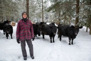 Rancher standing in front of herd of cows in the forest during the winter